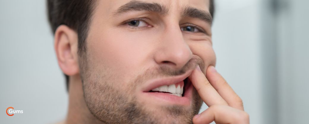 אבצס בחניכיים טיפול טבעי: איש בודק את שיניו נראה מוטרד. בצד שמאל למטה לוגו אתר "תת".